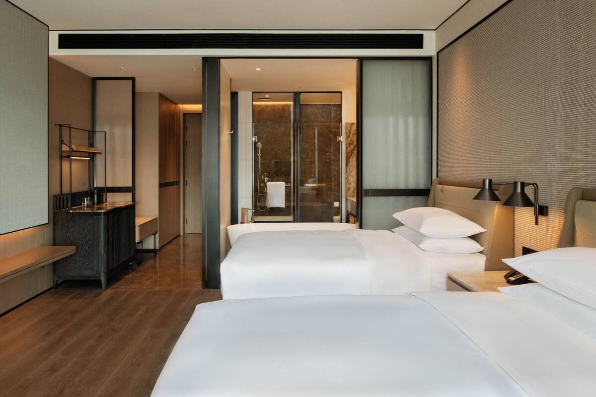 Une chambre d’hôtel avec un grand lit, un bureau, une chaise, une lampe et une porte coulissante donnant accès à la salle de bain.