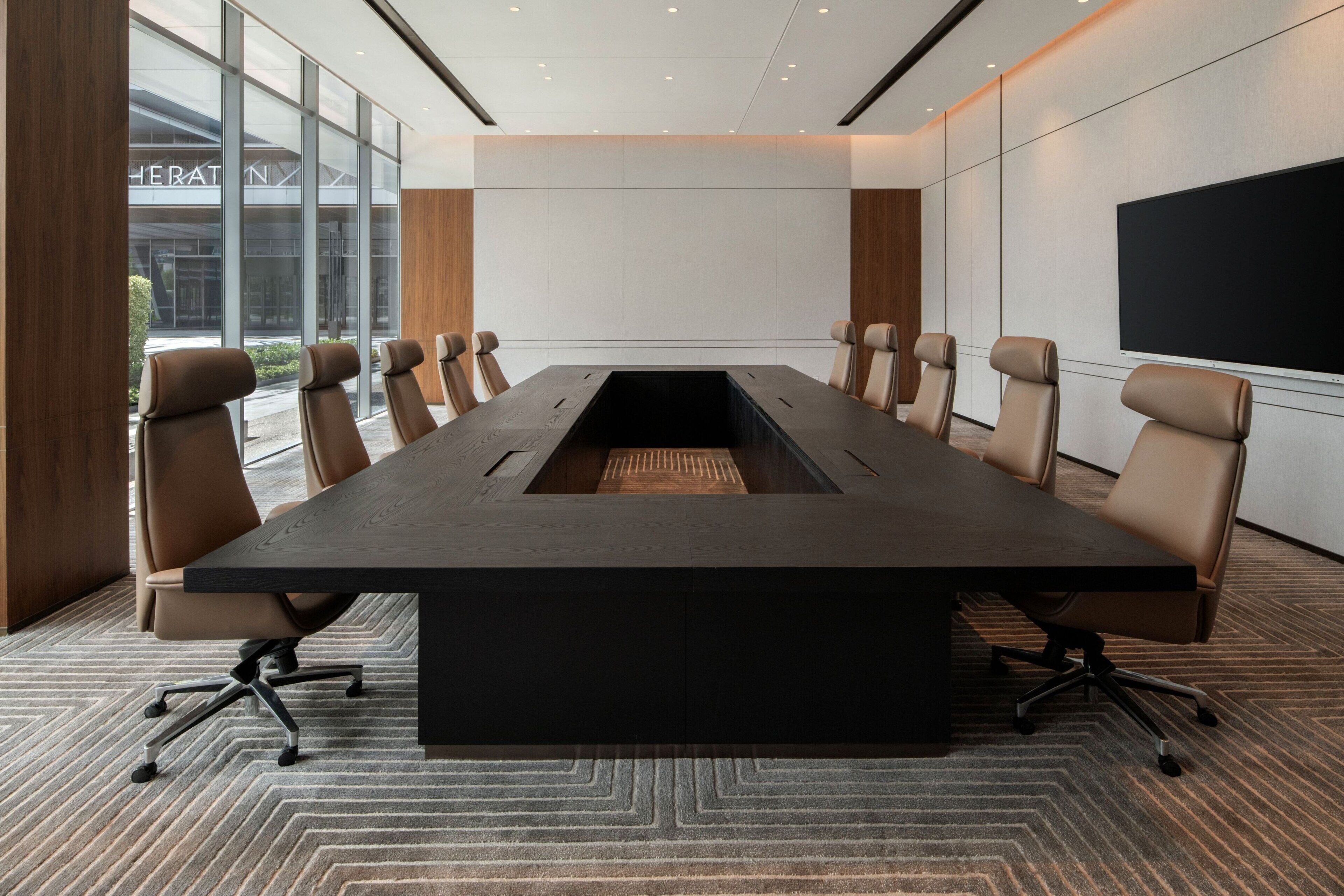 A conference room with a long table, six chairs, a large screen, and a view of the outside.