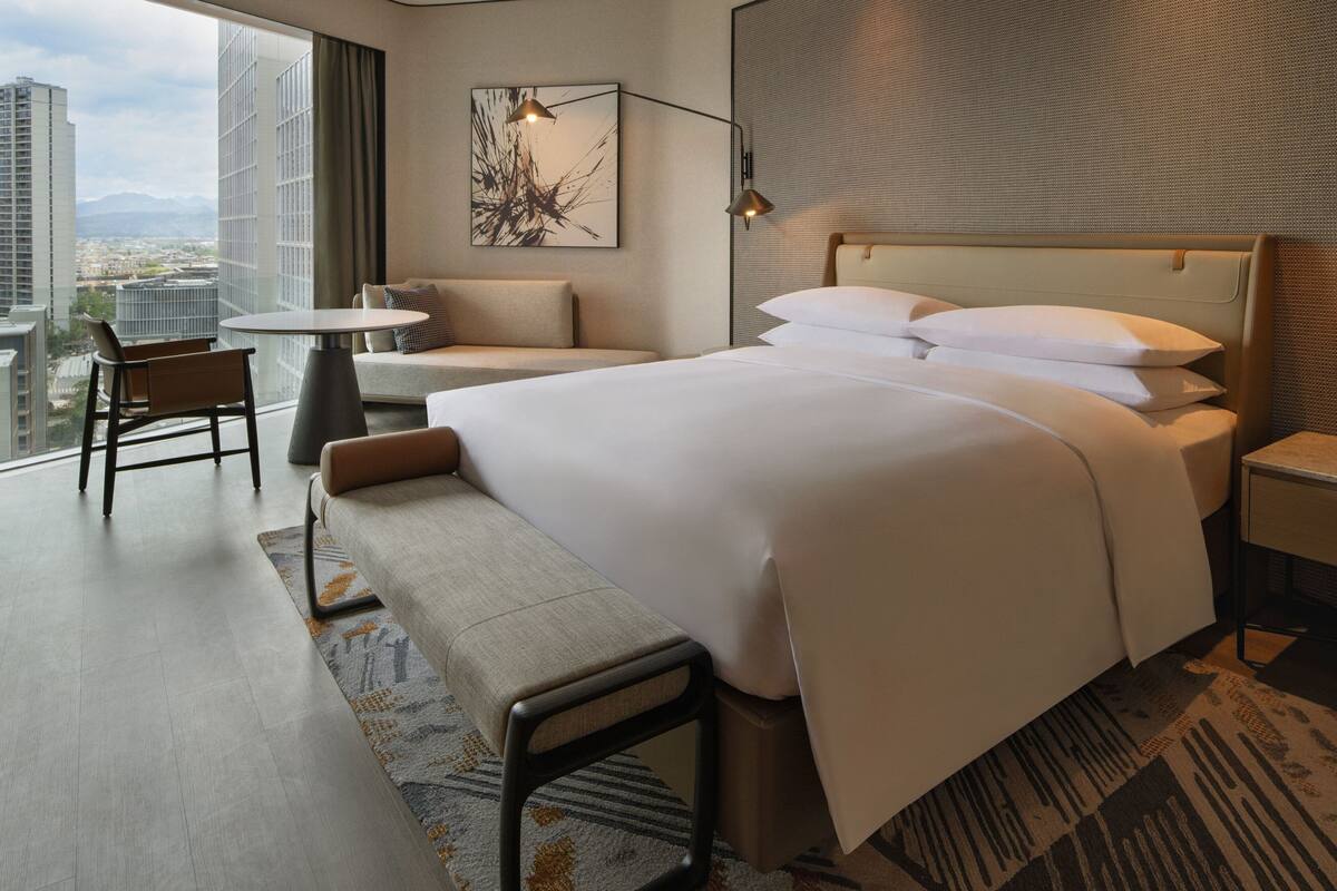 Une chambre d’hôtel moderne dotée d’un grand lit, d’un coin salon, d’une petite table et offrant une vue sur la ville.