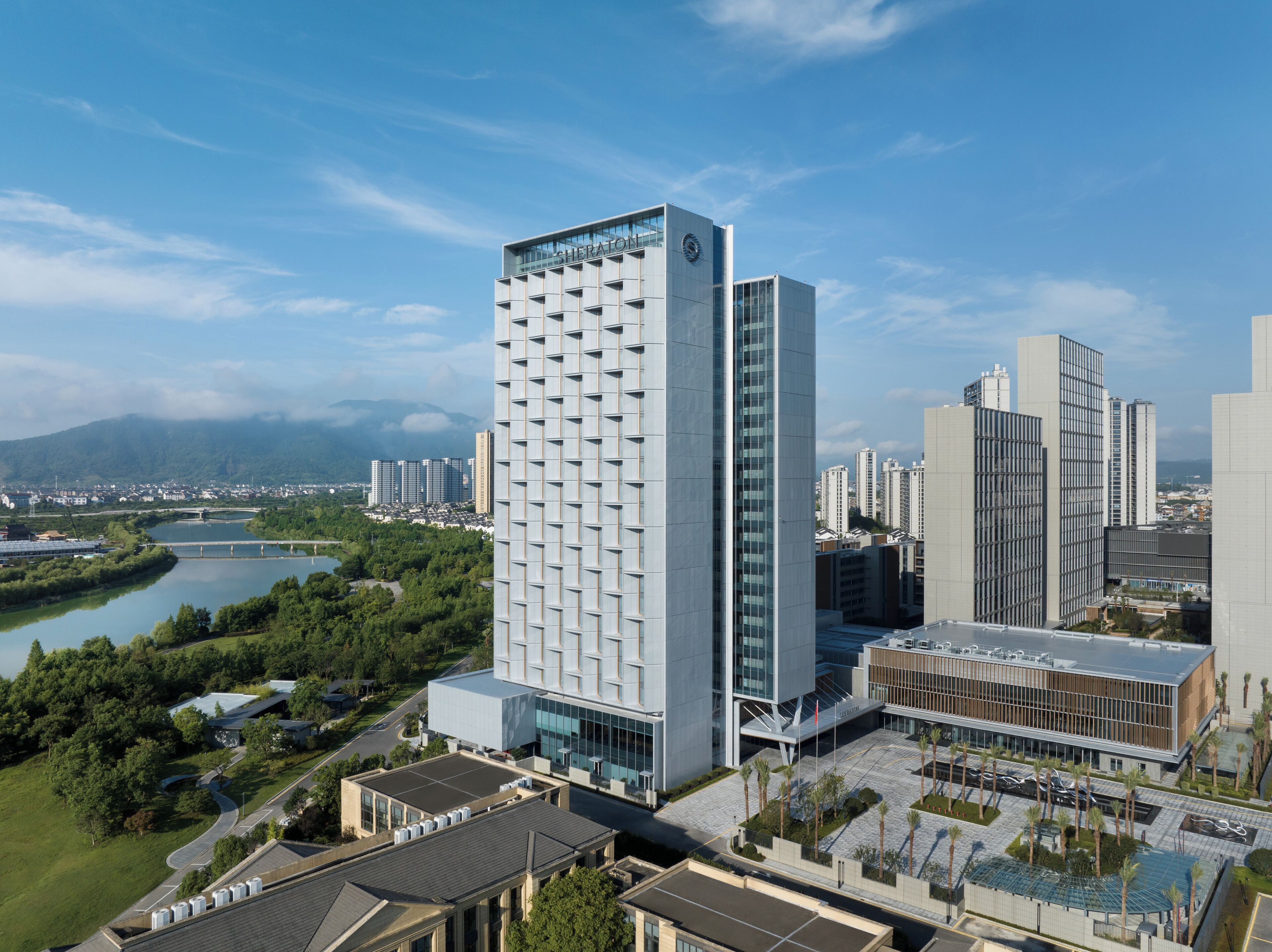 Ein modernes Hochhaus-Hotel mit einer markanten Glasfassade, gelegen in einer städtischen Umgebung mit Blick auf einen Fluss und Grünflächen.