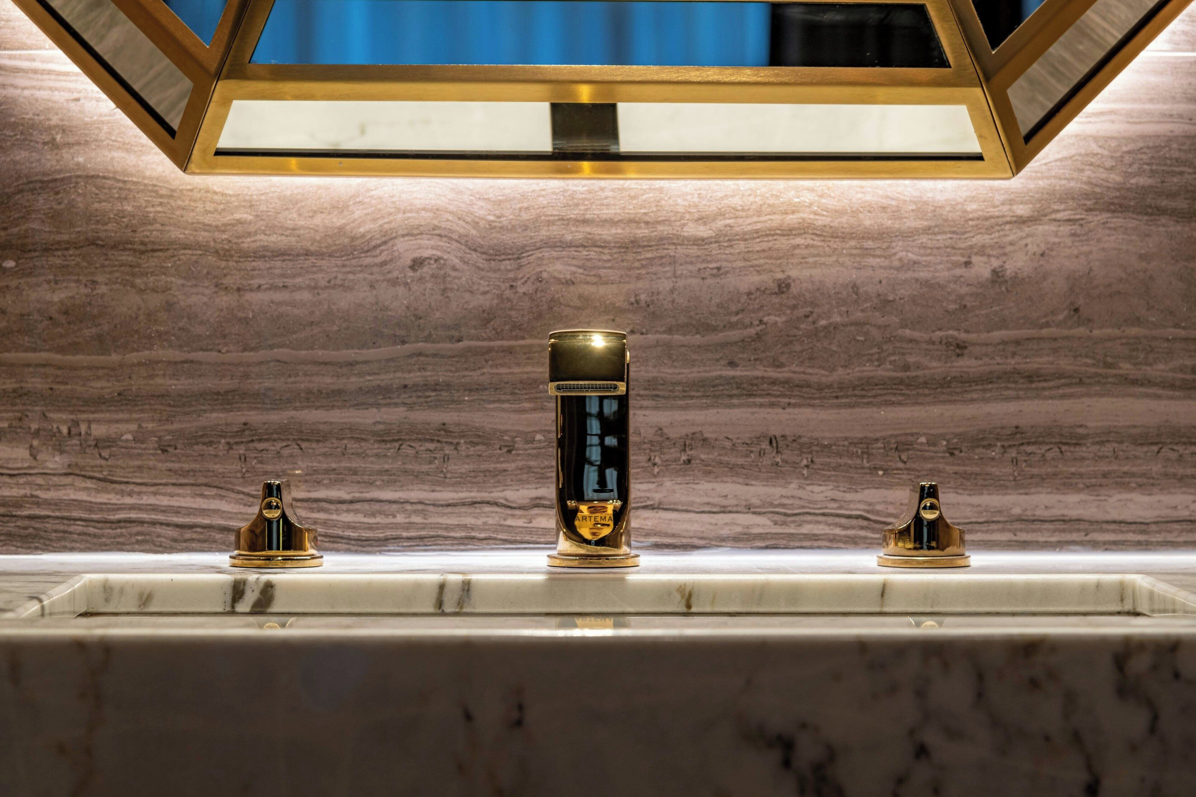 A bathroom with a marble countertop, a central faucet, and two side fixtures.