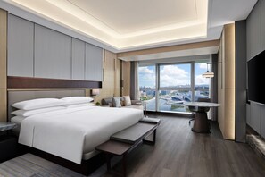A modern hotel room with a large bed, a bench, a dining table, and a TV. The room has a city view through large windows. - Zhuhai Marriott Hotel Jinwan (Zhuhai)