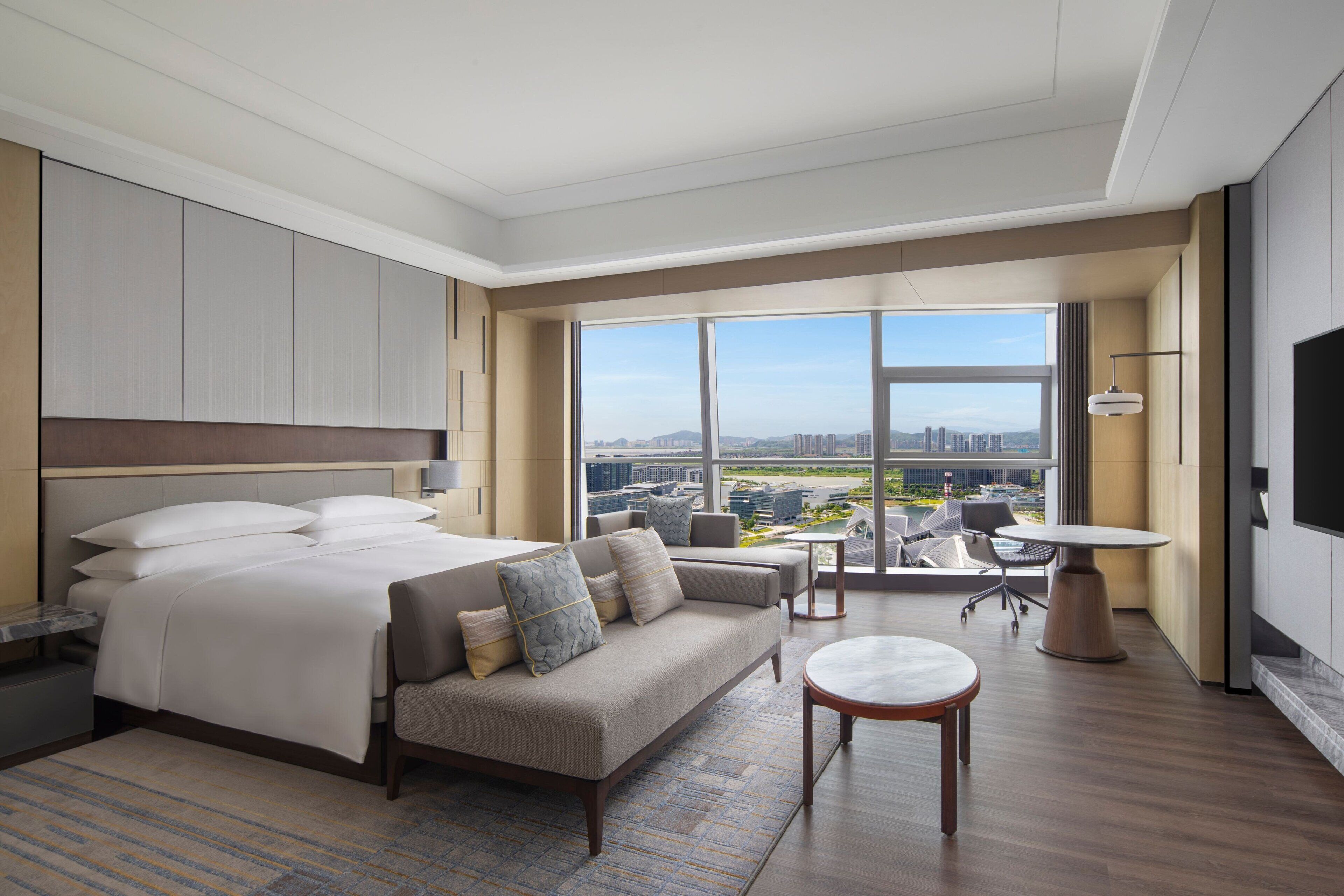 Una habitación de hotel moderna con una cama grande, un sofá, una mesa de comedor y vistas a la ciudad.