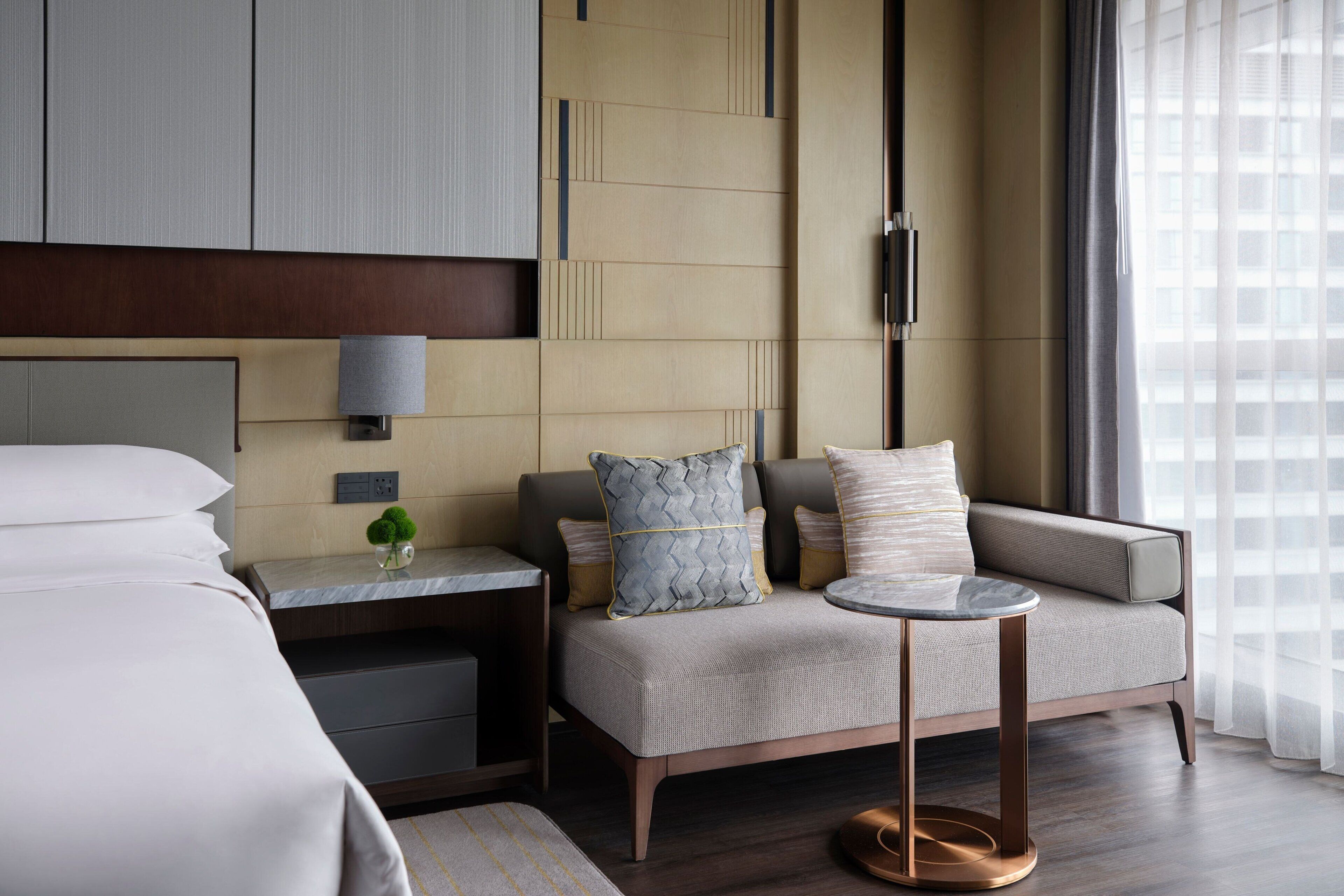 Una habitación de hotel moderna con una cama, un sofá, una mesita y una mesilla de noche.