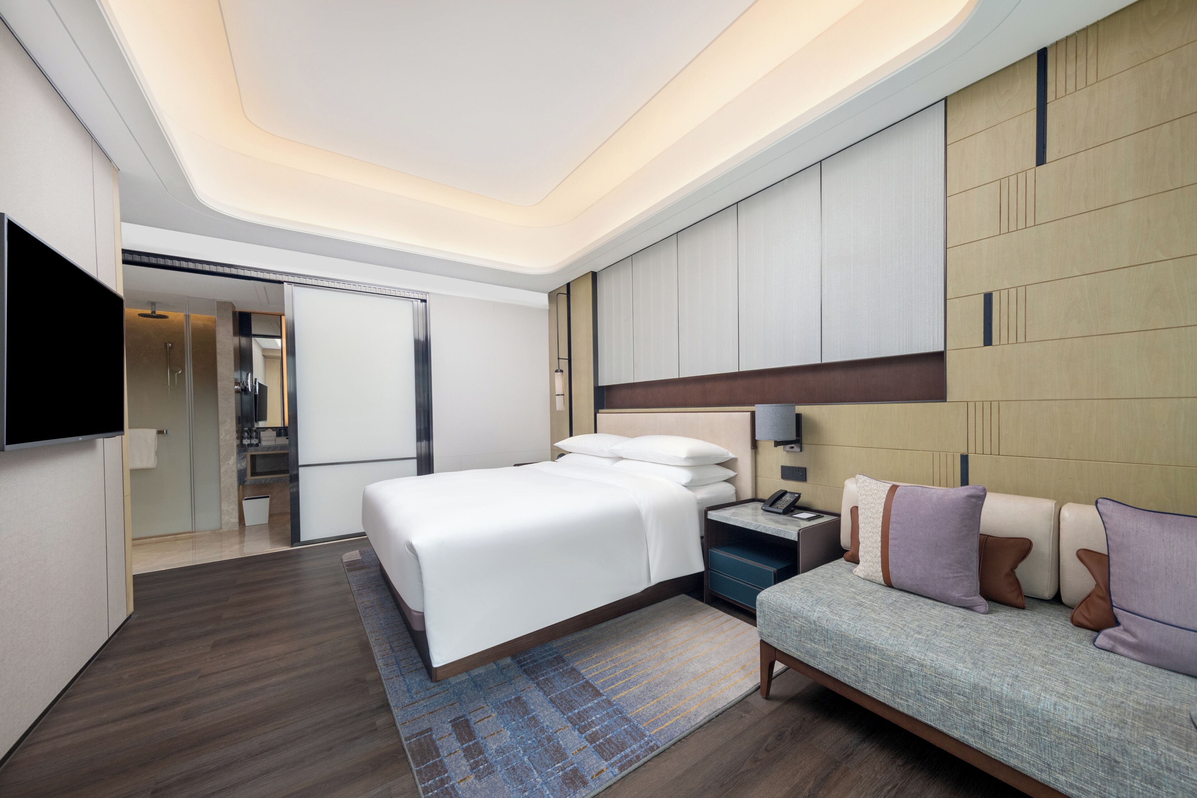 A modern hotel room with a large bed, a sofa, a flat-screen TV, and a walk-in closet.
