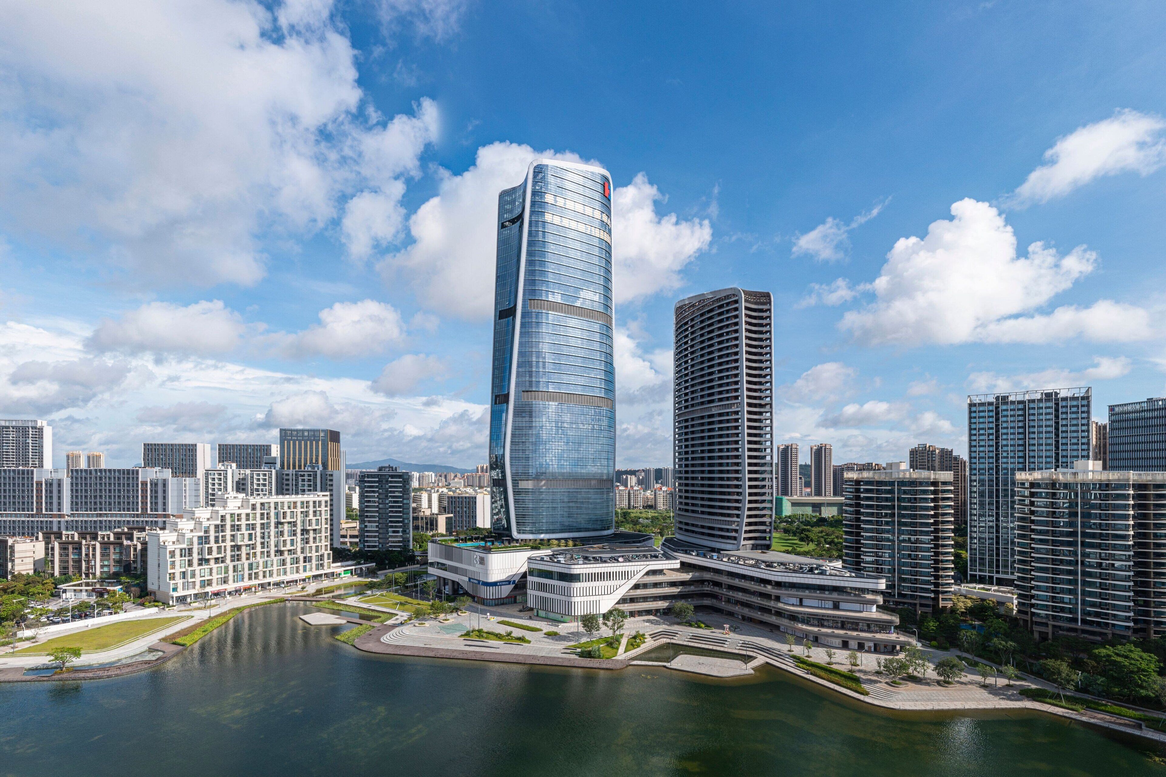 A modern cityscape with high-rise buildings, a central curved skyscraper, and a body of water.