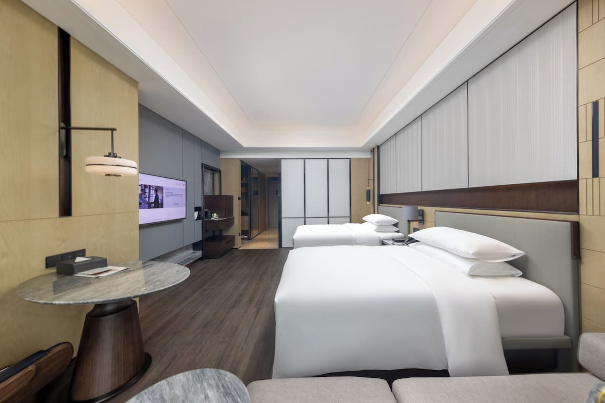 A modern hotel room with a large bed, a round table, and a TV on the wall.