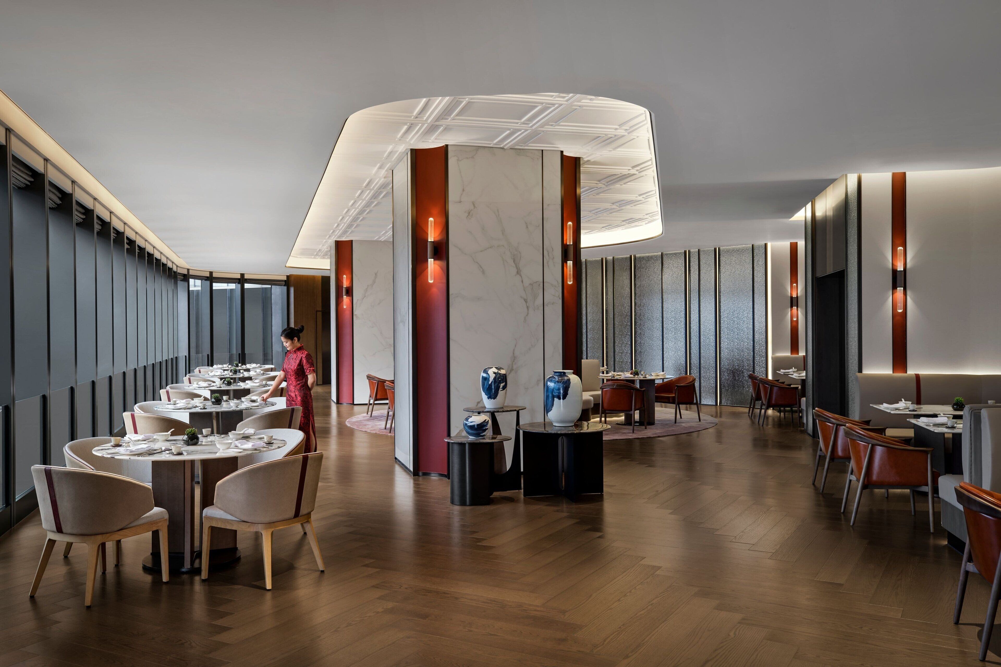 A modern restaurant with round tables, wooden flooring, and a central decorative column.