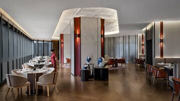 A modern restaurant with round tables, wooden flooring, and a central decorative column.