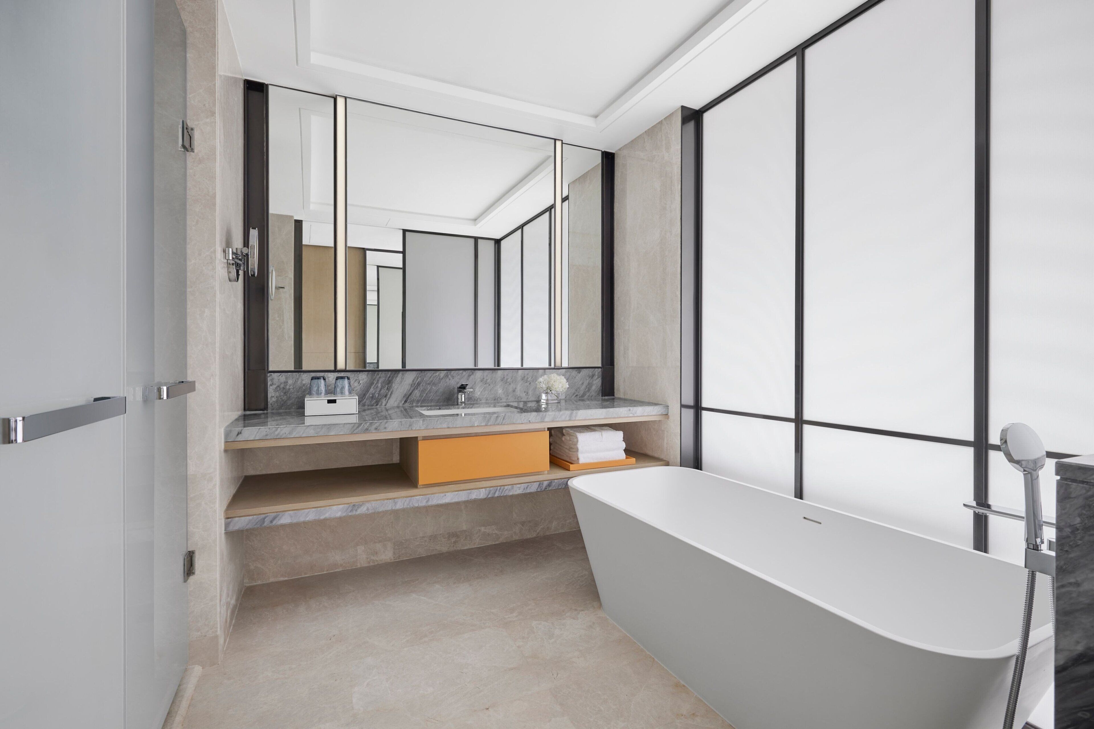 A modern bathroom with a freestanding bathtub, a large mirror, and a marble countertop.