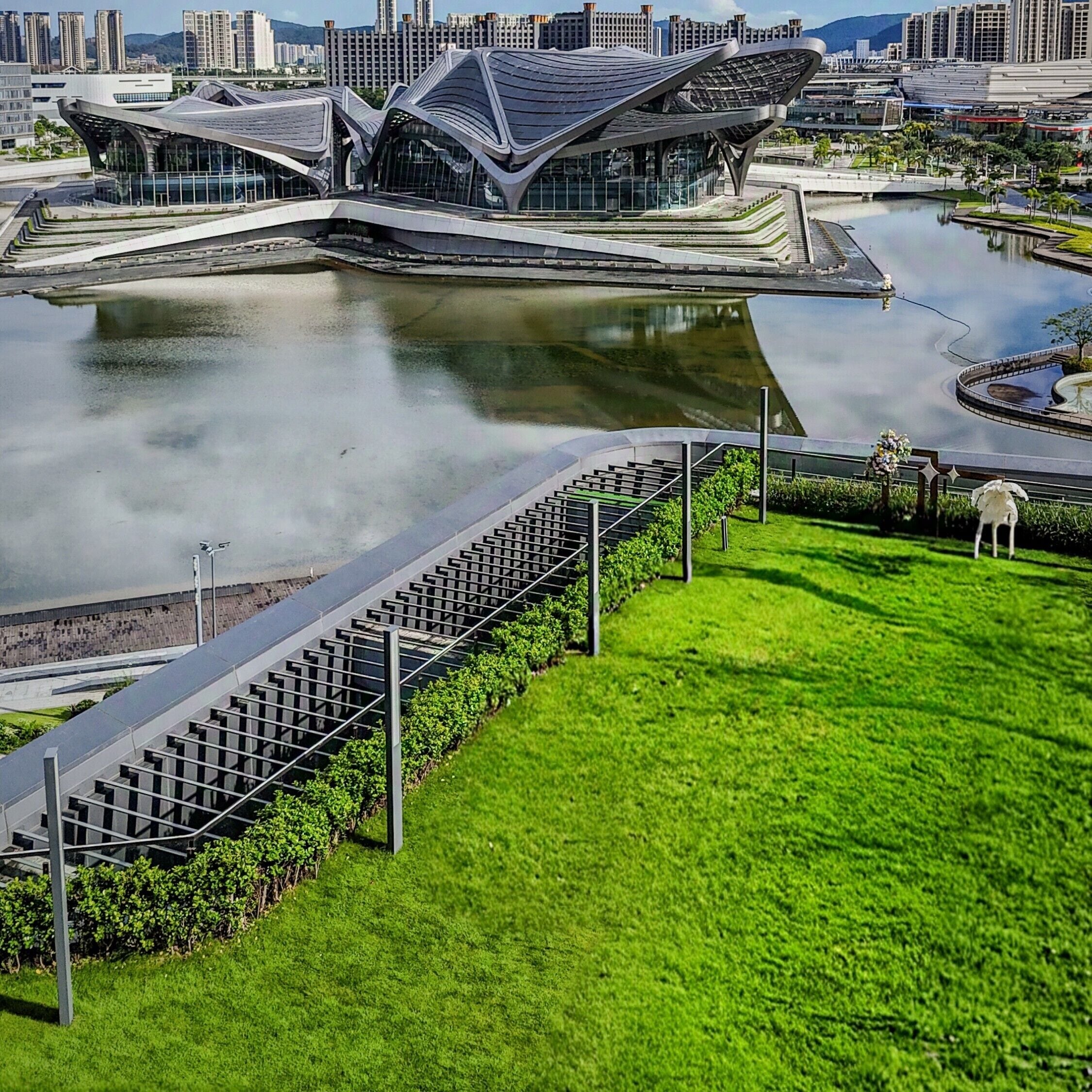 A modern building with a unique roof design, a water feature in front, and a green lawn area.