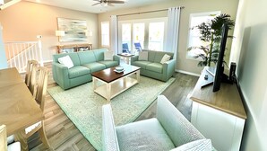 A spacious living room with a ceiling fan, two green sofas, a coffee table, and a TV on a wooden stand. - 2bd 2.5 bath with beach club, pools, hot tub, golf (Pensacola)