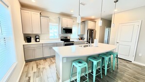 A modern kitchen with a central island, bar stools, and built-in appliances. - 2bd 2.5 bath with beach club, pools, hot tub, golf (Pensacola)