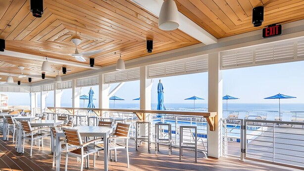 A spacious outdoor dining area with tables and chairs, large windows offering ocean views, and an exit sign. - 2bd 2.5 bath with beach club, pools, hot tub, golf (Pensacola)