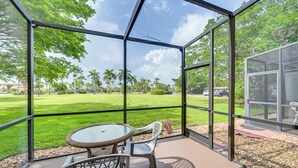 Un patio techado con una mesa y sillas de vidrio, con vistas a un césped cuidado y árboles.