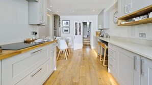 A modern kitchen with white cabinetry, a wooden countertop, and a dining area with white chairs. - I Came To Boogie (London)