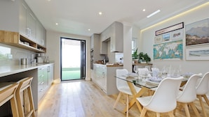 A modern kitchen with white cabinets, a glass dining table, and a view to the outside. - I Came To Boogie (London)
