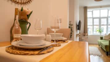 A dining table set with white plates, bowls, and wine glasses, a bottle of wine, and a vase with flowers.