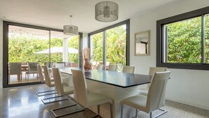 Un espace de salle à manger moderne avec une cloison en verre, des chaises blanches, une table noire et des luminaires suspendus.