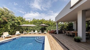 Un espace piscine extérieur moderne, doté de chaises longues et de parasols, et entouré de verdure.