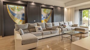 Un salon moderne avec un canapé d’angle, une table basse en verre et des panneaux décoratifs en vitrail sur le mur.