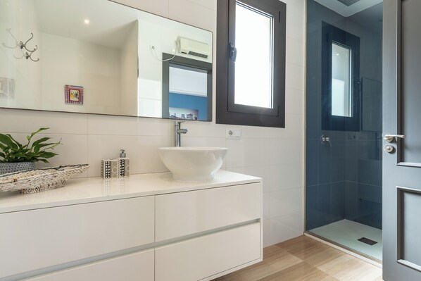 A modern bathroom with a white vanity, a large mirror, a white sink, and a glass-enclosed shower.
