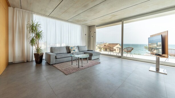Un salon moderne avec un canapé gris, une table basse en verre et une grande fenêtre donnant sur la mer.