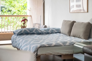 A bed with patterned bedding, a chair, a potted plant, and a framed picture on the wall.