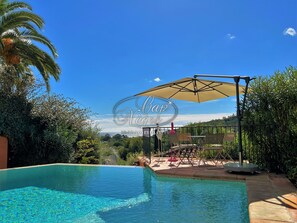 Une piscine d’un bleu éclatant, agrémentée d’une pergola et de chaises longues, entourée d’une végétation luxuriante et offrant une vue sur les collines.
