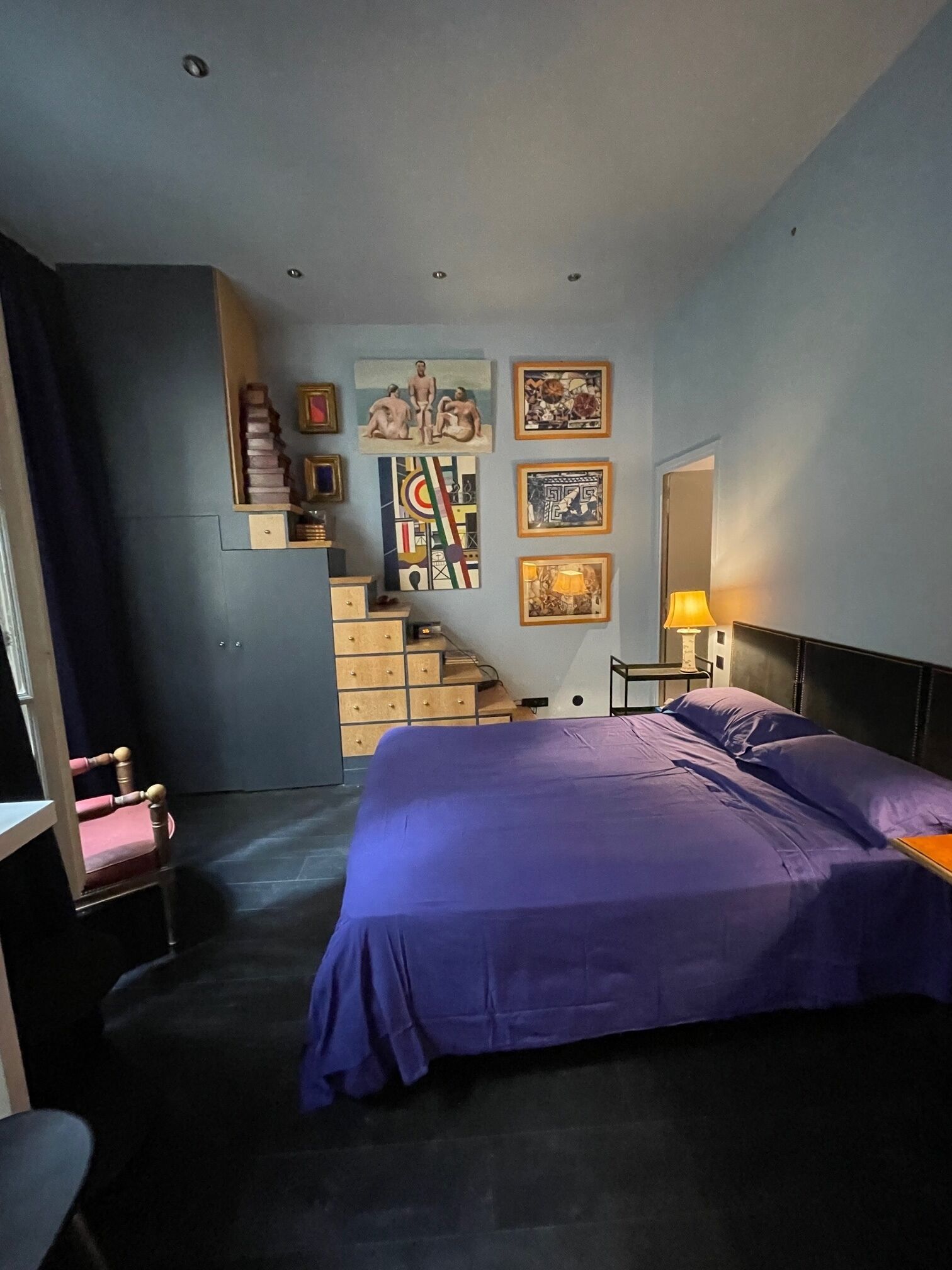 Une chambre à coucher comprenant un lit, une chaise, une commode, un escalier et des œuvres d’art murales.