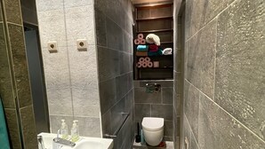 Et moderne badeværelse med en hvid vask, toilet og en hylde med håndklæder og toiletartikler.