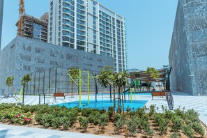 A modern urban plaza with a swimming pool, exercise equipment, and greenery.