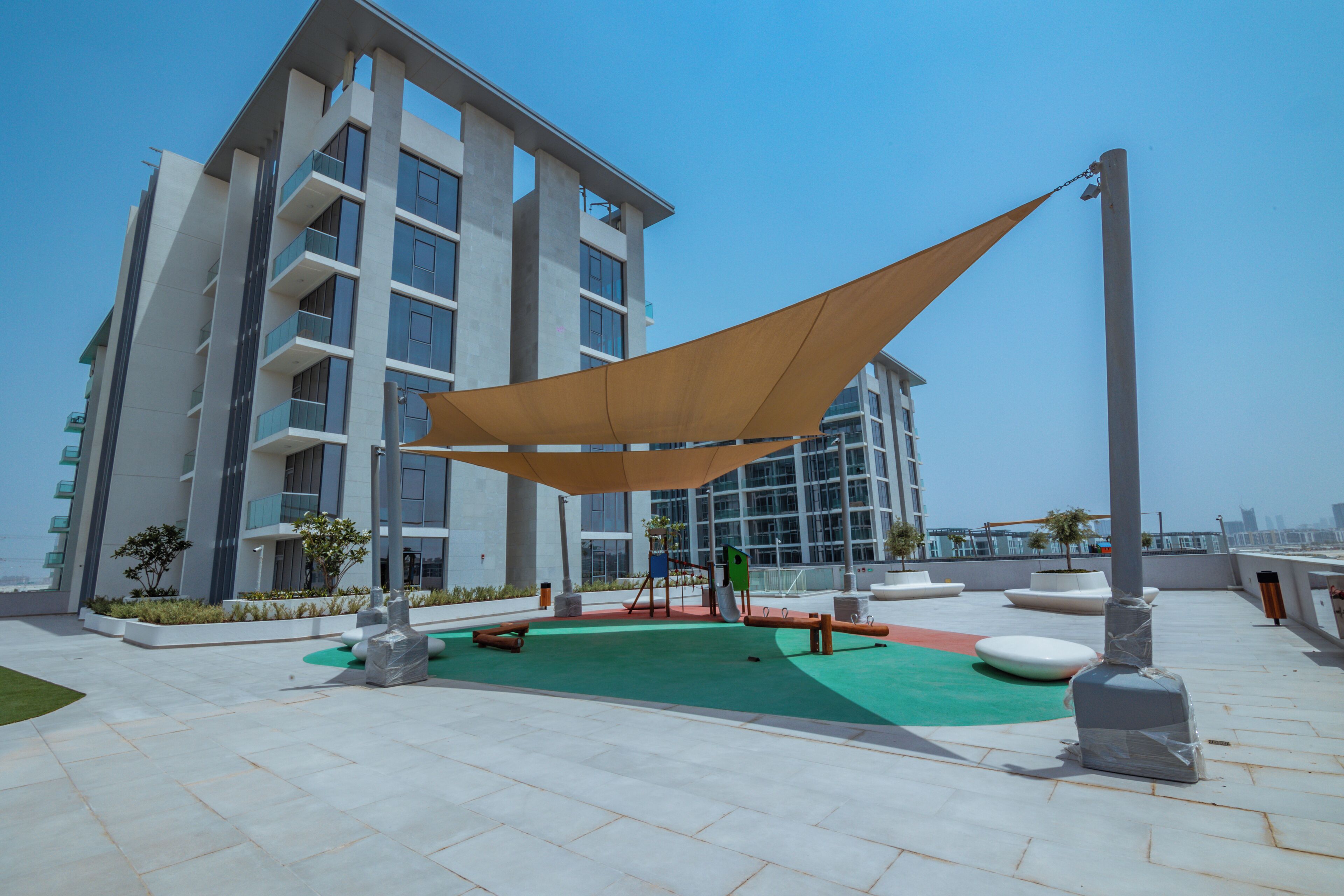 A rooftop terrace with a large shade sail, outdoor seating, and a view of a modern building.