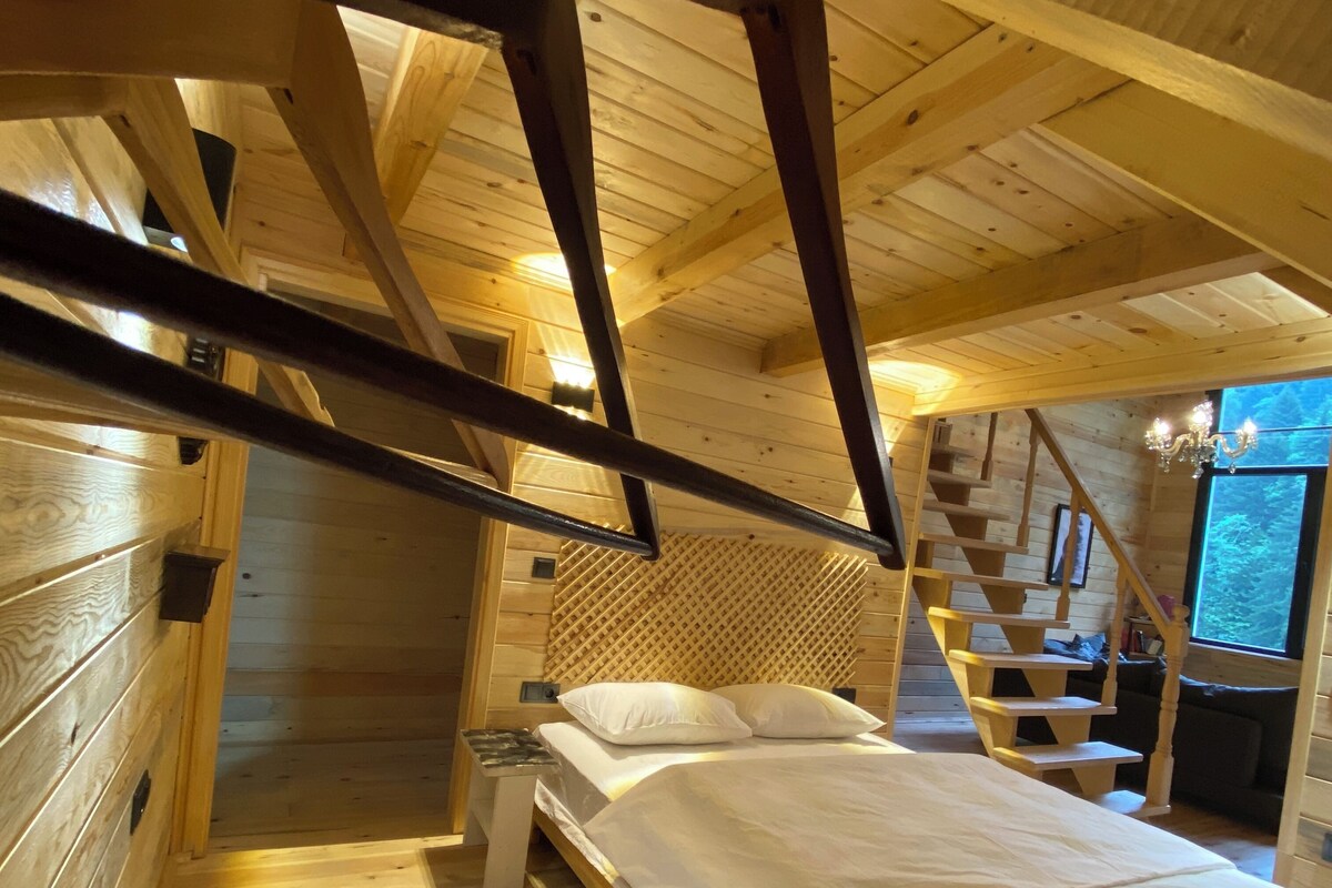 Camera da letto in una baita di legno, con un letto, un comodino, un tappeto colorato fatto a mano e una scala che conduce a un livello superiore.