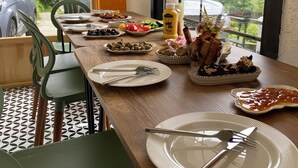 A dining table set with plates, cutlery, and various dishes, with a view of greenery and parked cars outside. - Nanu's Ayder Bungalow ve Kahvaltı (Rize)