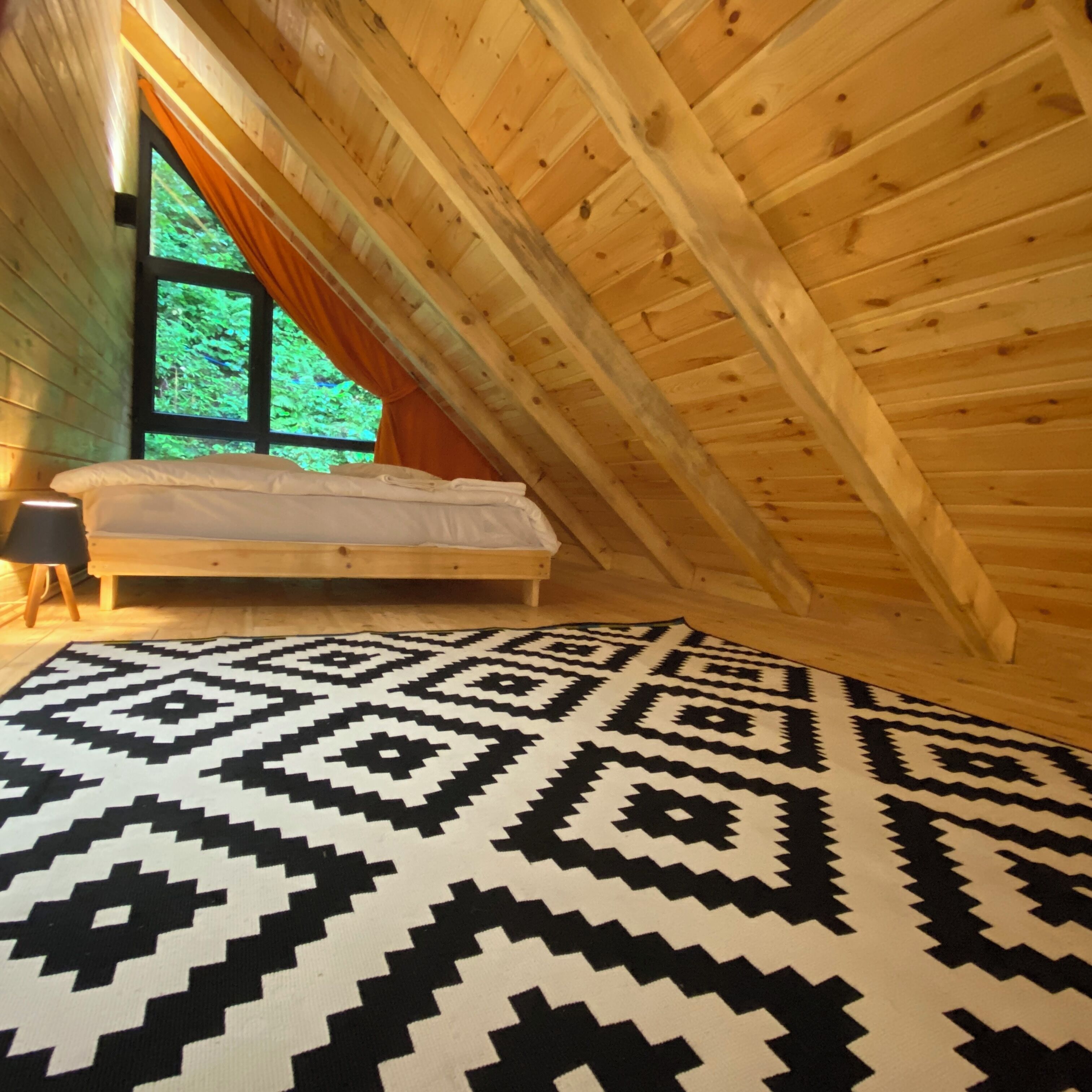 A cozy attic bedroom with a bed, a nightstand, and a window with curtains.
