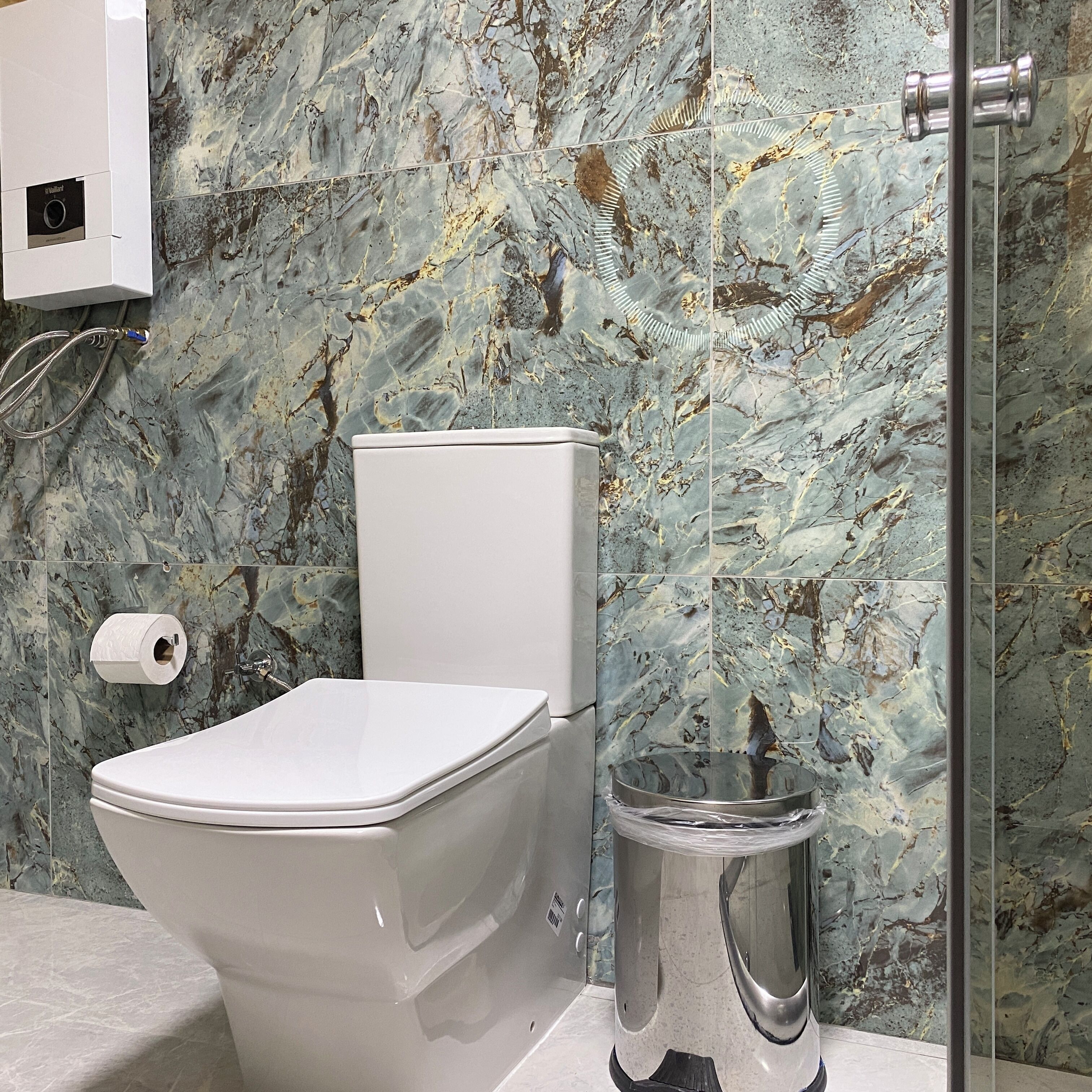 A bathroom with a toilet, a marble wall, and a shower area.