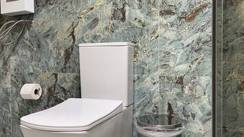 A bathroom with a toilet, a marble wall, and a shower area.