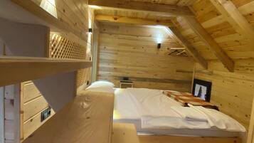 Habitación tipo cabaña de madera con literas, una mesita, un banco y un techo inclinado con tragaluz.