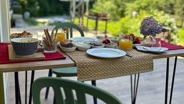 A breakfast table set outdoors with various dishes, a view of green hills, and a power line in the background. - Nanu's Ayder Bungalow ve Kahvaltı (Rize)