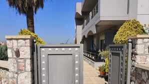 Une entrée fermée par un portail, avec un mur en pierre et un portail en métal, qui mène à un bâtiment moderne doté de balcons et de plantes en pot.