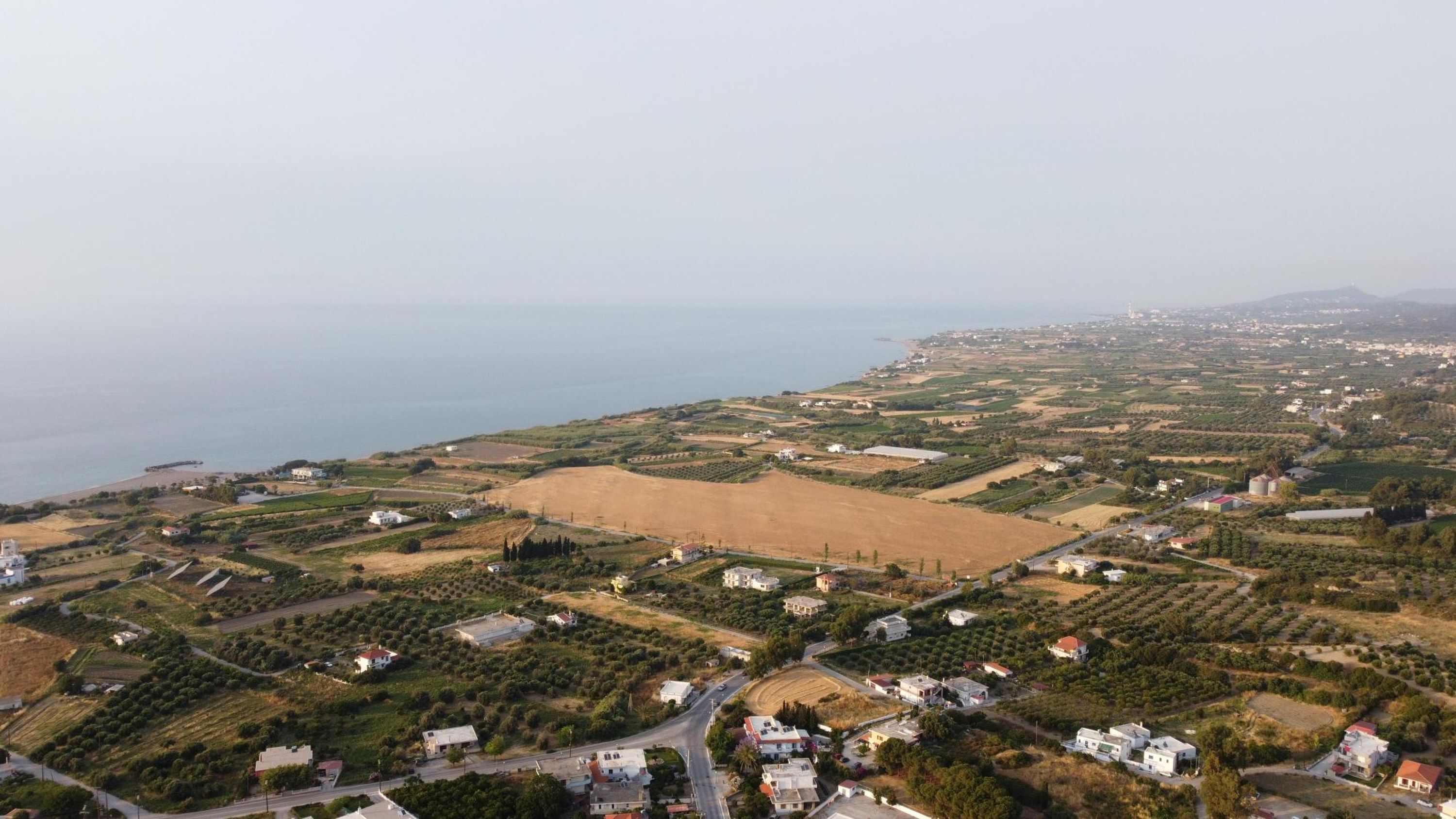 An aerial view of a coastal town with residential areas, agricultural fields, and a coastline.