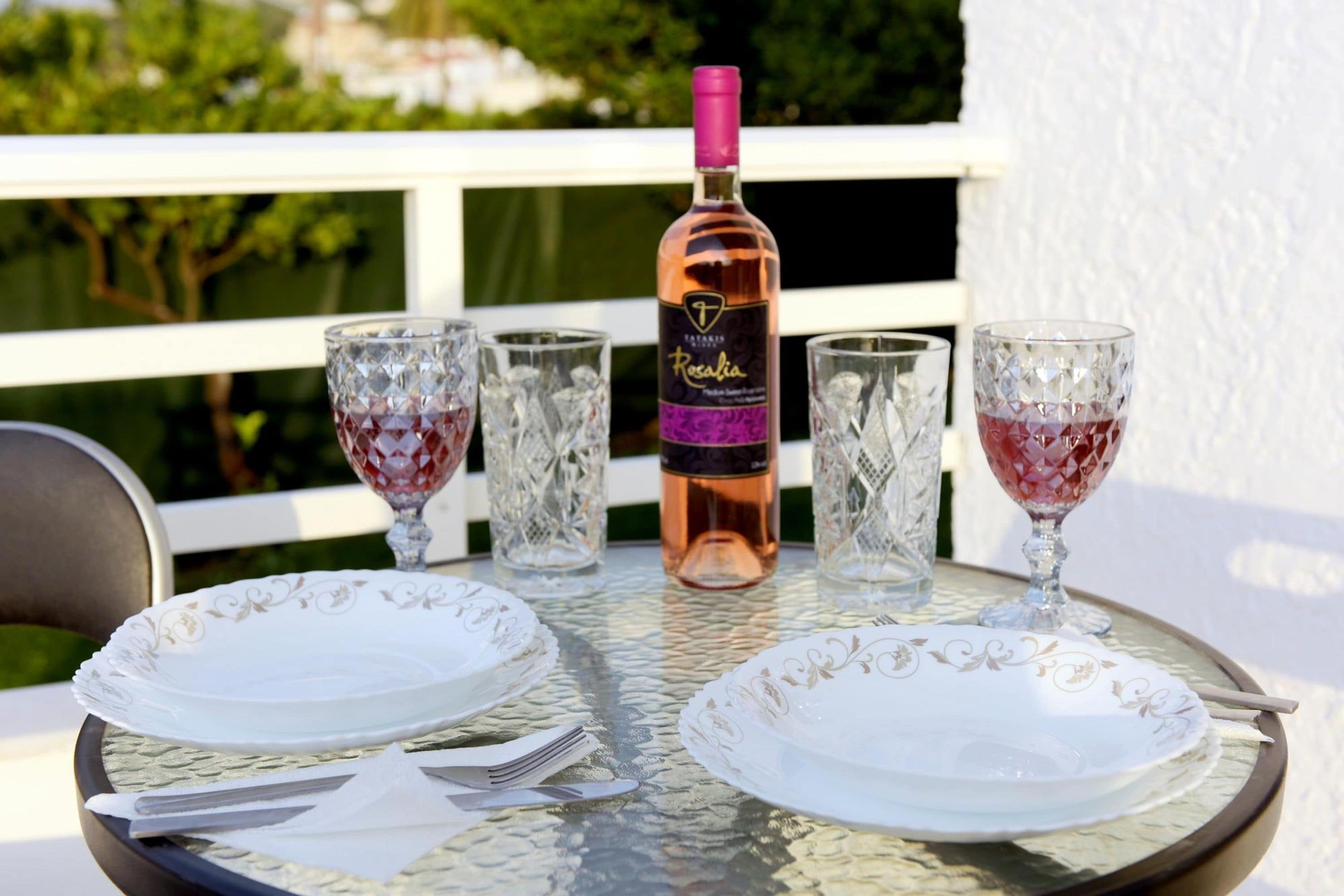 A table set with white plates, cutlery, and crystal glasses, with a bottle of rosé wine in the center.