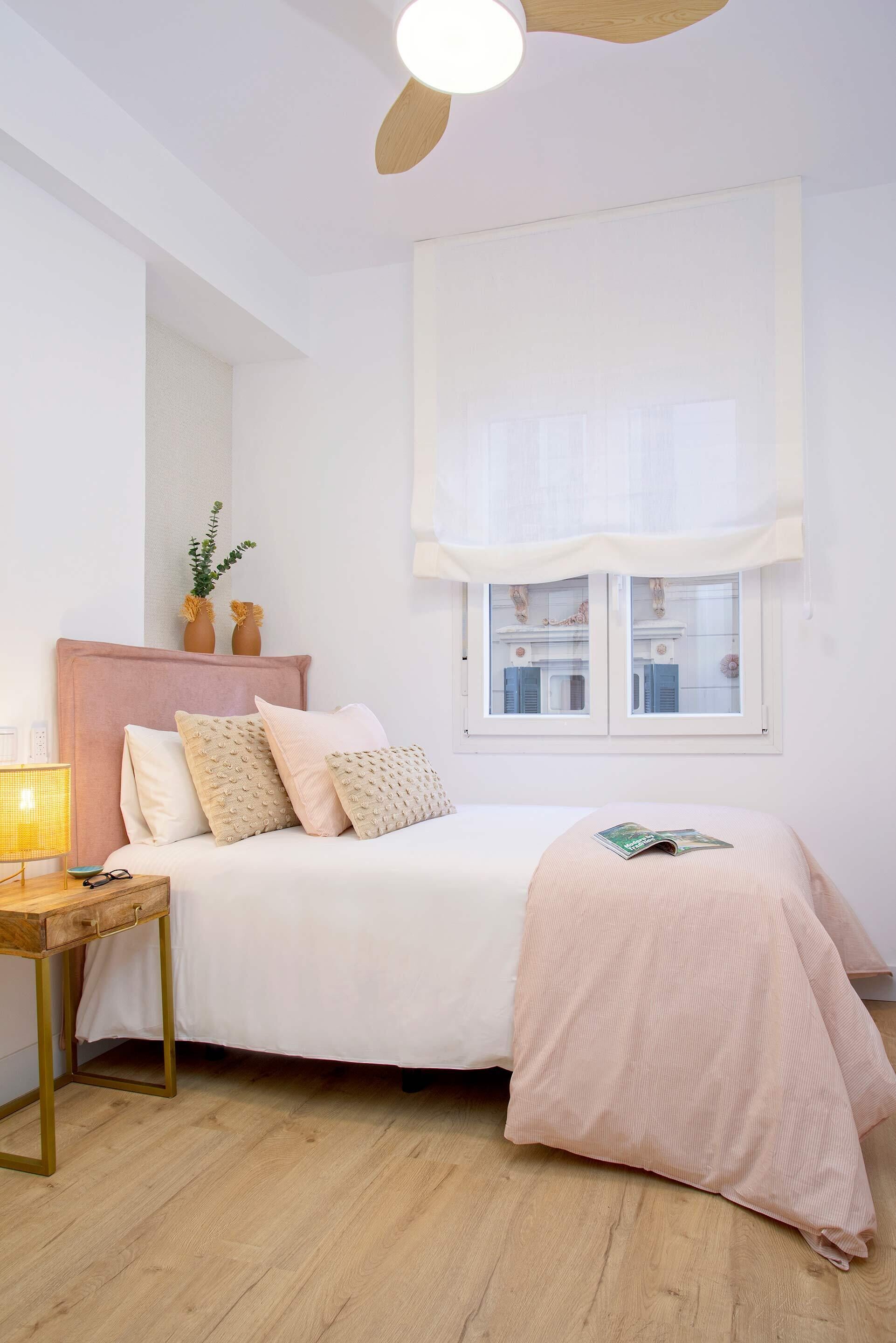 Un dormitorio con cama, mesita de noche, lámpara, ventana y ventilador de techo.