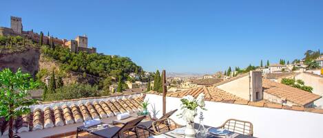 A rooftop terrace with a table set for dining, overlooking a historic cityscape with a castle.