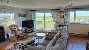 A spacious living room with a large window offering a view of the countryside, a comfortable sofa set, a television, and a fireplace. - Family Escape | Garden, Parking, Pet friendly (Salcombe)