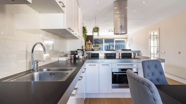 A modern kitchen with a central island, stainless steel appliances, and a grey upholstered chair. - 2 bedroom apartment in breukelen (Breukelen)