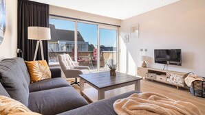 A modern living room with a sofa, a coffee table, a TV, and a balcony with outdoor furniture. - 2 bedroom apartment in breukelen (Breukelen)