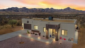 A modern two-story house with a flat roof, large windows, and a garage. It is surrounded by a gravel driveway and features outdoor lighting. - New Hillside Home overlooking Santa Cruz River Valley in Rio Rico near Tubac (Rio Rico)