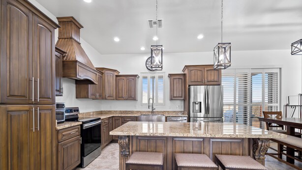 A spacious kitchen with wooden cabinets, a large island with bar stools, stainless steel appliances, and pendant lighting. - New Hillside Home overlooking Santa Cruz River Valley in Rio Rico near Tubac (Rio Rico)